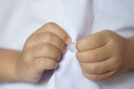 closeup hand of child student or kid learning and trying for wear white shirt button or unbutton on...