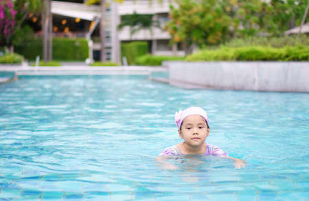 Asian child cute or kid girl wear swimming suit and cap on swimming pool and smiling with happy fun in water park for learning and training or refreshing and relax with exercise on summer holidayの写真素材
