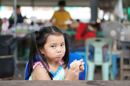 Asian child cute or kid girl hungry and enjoy eating corn boil for vegetable food or fruit snack with fiber vitamin to health diet and happy smiling in fresh market on street travel and relaxの写真素材