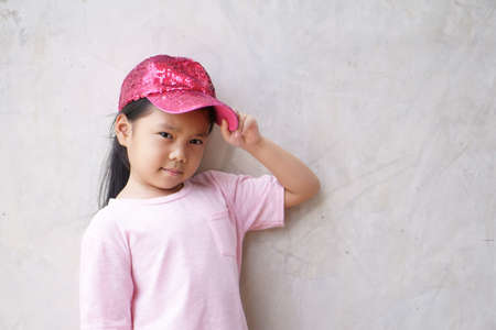 Asian child cute or kid girl smiling and happy with sport dancer and hand on hat with wear pink shirt for beauty fashion on summer holiday travel or party and loft gray cement wall backgroundの写真素材