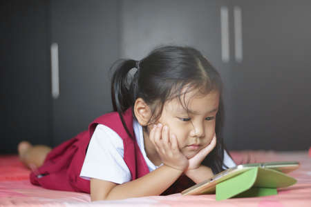 Asian child cute or kid girl student wear school uniform looking and play tablet or smartphone on...