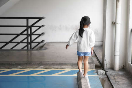 Asian child or kid girl lonely and walk alone with touchy or have problems in car parking or parking lot to wait for the parents or family on city street at nursery or kindergarten and pre schoolの写真素材