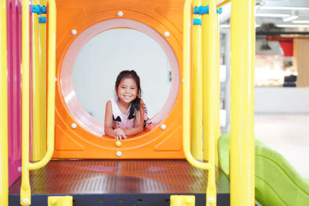 Asian child or kid girl smiling playing colorful tunnel on slider with happy fun or cheerful enjoy on holiday relax with exercise at playground or amusement public park and nursery kindergarten schoolの写真素材