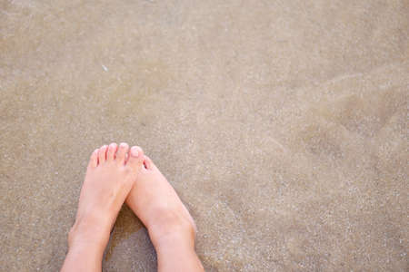 foot or feet and leg of child or kid on sand beach and sit with sea water wave and alone or lonely...