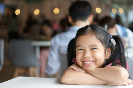 Asian child cute or kid girl smile white teeth and happy or cheerful with sit on table in restaurant or food court to lot of people at nursery school or mall for relax and dental background with spaceの写真素材