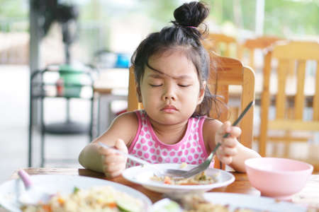 Asian child cute or kid girl anorexia or sad and bored food or boredom with frown on wood table for breakfast or lunch eating at restaurant on preschool or nurseryの写真素材