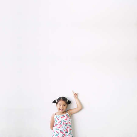 Asian child cute or kid girl thinking smiling with finger point on top for new idea and imagination or creativity education with happy at nursery preschool on white wall background and space isolatedの写真素材