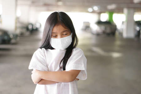 Asian child close eye or kid girl wear N95 cloth face mask for close mouth and sick on nose with cold cough and protect PM 2.5 dust or influenza covid-19 virus and bacteria from smoke and crossed armsの写真素材