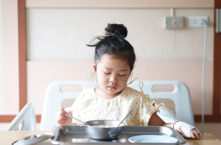Asian child patient or kid girl Influenza A sick and sad with cry to want encouragement with salt water in hand blood vessels on bed at hospital room for treatment healthcare with lunch food and boredの写真素材