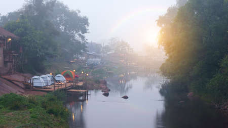 camping tent and cabin cottage on warm sunlight in rainbow and stream or river with rock in green jungle at sapan for summer holiday fresh relax and vacation travel trip on cool nature morning mistの写真素材