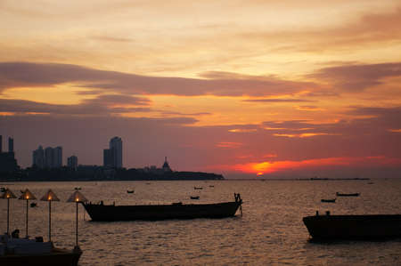 sea and city restaurant with marine fishing boat on golden sky twilight or evening sunset with warm light by red sun and lamp in pattaya at Thailand for holiday travel and relax dinner with peopleの写真素材