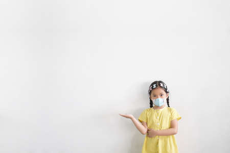 Asian child or kid girl wear N95 mask for close mouth nose with cold cough sick and protect influenza covid-19 virus or PM2.5 dust bacteria by smoke and hand point present on white space backgroundの写真素材
