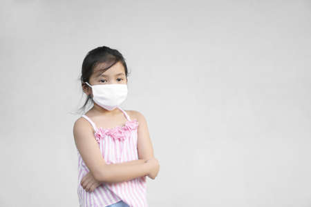 Asian child sad or kid girl lonely wear cloth face mask for close mouth nose and cold cough sick to protect influenza covid-19 or coronavirus and PM 2.5 dust with bacteria by smoke and crossed armsの写真素材