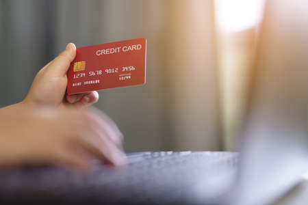 hand of child or kid holding credit card for online shopping and electronic payment from home by internet banking or digital and e-wallet on computer notebook with warm sunlightの写真素材