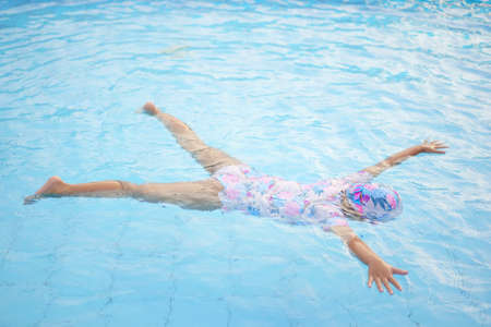 Asian child cute or kid girl practicing floating in water by spread arms and legs to pretends...