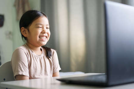 Asian child student or kid girl smile enjoy and laugh on computer notebook for e-learning communication or study online and people learn from home to playing laptop for education by back to schoolの写真素材