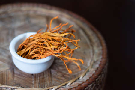 Dry cordyceps militaris in a white bowl with wooden background. Orange medical mushroom for good...
