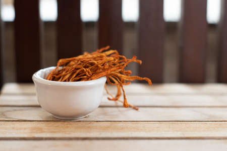 Dry cordyceps militaris in a white bowl with wooden background. Orange medical mushroom for good health.の写真素材