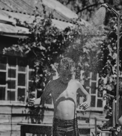 Boy under a shower outdoors in hot dayの写真素材