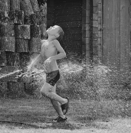 Boy under a shower outdoors in hot dayの写真素材