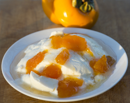 Tasty and healthy breakfast. Homemade yogurt with pieces of fresh persimmon fruits on a plate の写真素材