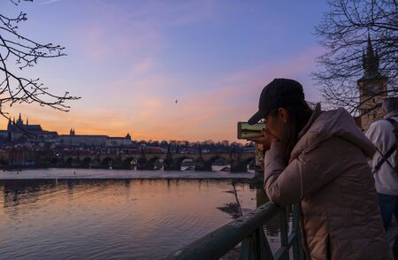 PRAGUE / CZECH REPUBLIC - MARCH 29, 2019: Girl shoots sunset on a telephone in Prague