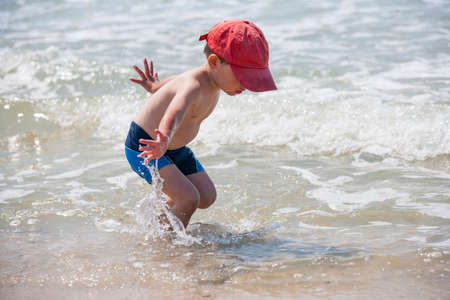 A little boy on the beach, playing with the waves, summer time. Concept of relaxation and a healthy lifestyleの写真素材