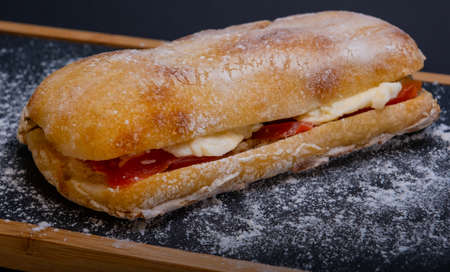Ciabatta sandwich with mozzarella cheese and tomatoes on a wooden trayの写真素材