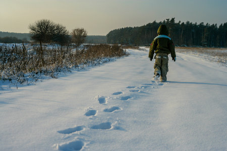 Little boy back view walking through the nature. Footprints in the snow. Healthy active life