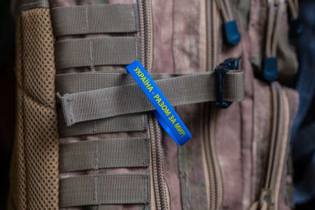 Yellow-blue bracelet with an inscription in Ukrainian: "Ukraine - together for peace!" Prevention of hostilities in Ukraine. peace concept. Military backpack of khaki color. Camouflage backpack. Military equipment is special, close upの写真素材