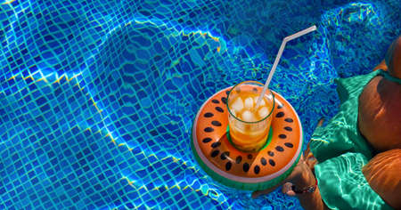Cold refreshing drink with ice and a straw in the inflatable ring in shape of watermelon in a...