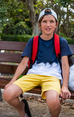 Cute smiling boy in a hat looking at the camera. Resting on a bench on a hot summer dayの写真素材