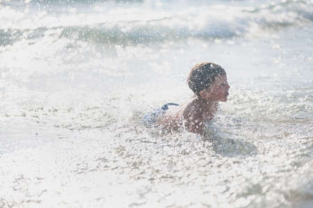 A little boy on the beach, playing with the waves, summer time. Concept of relaxation and a healthy...