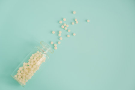 Alternative homeopathy medicine concept. Homeopathic globules scattered from a clear glass bottle on light blue background, copyspace for text. Health care and pills conceptの写真素材