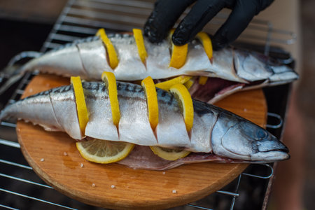 Grilled mackerel fish with herbs and lemon slices, top view. The process of cooking fish outdoors. Tasty and fresh food, picnic, party, outdoor recreationの写真素材