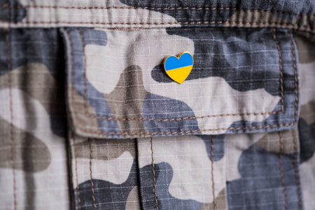 Metal badge with the flag of Ukraine in the shape of a heart on military jacket. Support for Ukraine. War in Ukraine. Ukraine flag themeの写真素材