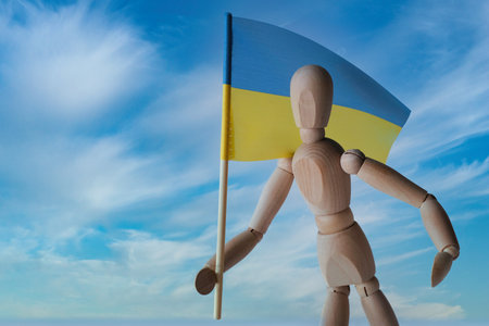 Patriotic wooden mannequin holding the Ukrainian blue and yellow flag against the sky. Stand with Ukraine. Independence Day - 24 of Augustの写真素材
