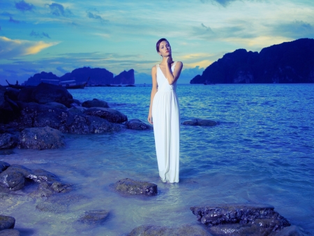 Beautiful lady in a white dress on a rocky shoreの写真素材