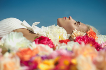 Beautiful blonde young woman lying in flowersの写真素材
