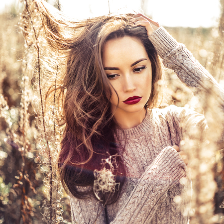 Outdoor fashion photo of young beautiful lady in autumn landscape with dry flowers