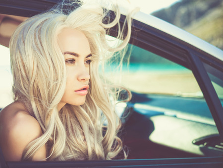 Atmospheric outdoors fashion portrait of beautiful blonde in car on the beachの写真素材