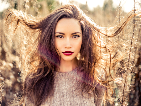 Outdoor fashion photo of young beautiful lady in autumn landscape with dry flowers. Knitted sweater, wine lipstick. Warm Autumn. Warm Springの写真素材