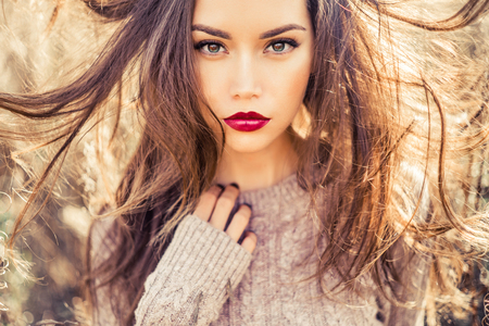 Outdoor fashion photo of young beautiful lady in autumn landscape with dry flowers. Knitted sweater, wine lipstick. Warm Autumn. Warm Springの写真素材