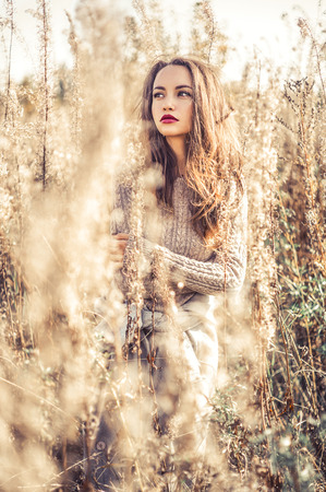 Outdoor fashion photo of young beautiful lady in autumn landscape with dry flowers. Knitted sweater, wine lipstick. Warm Autumn. Warm Springの写真素材
