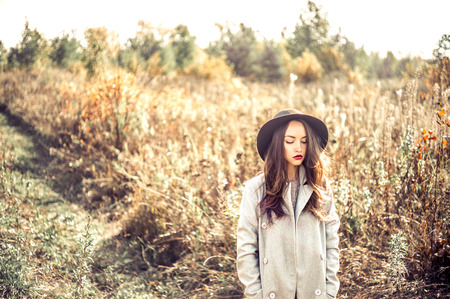 Outdoor fashion photo of young beautiful lady in autumn landscape with dry flowers. Gray coat, black hat, wine lipstick. Warm Autumn. Warm Springの写真素材