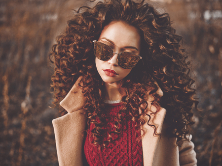 Outdoor fashion photo of young beautiful lady in autumn landscape. Beige coat, knitted sweater, wine...