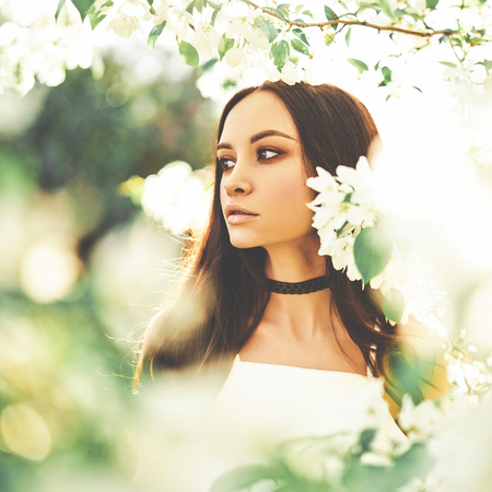 Outdoor fashion photo of beautiful young woman surrounded by flowers of apple-tree. Spring blossom. Summer vibesの写真素材