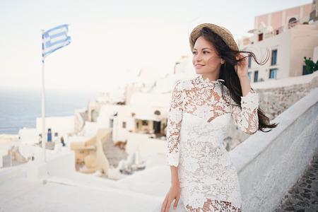 Happy woman in white dress and straw hat enjoying her holidays on Santorini island. View on Aegean sea from Oia. Europe summer travel destination. Greek Islandsの写真素材