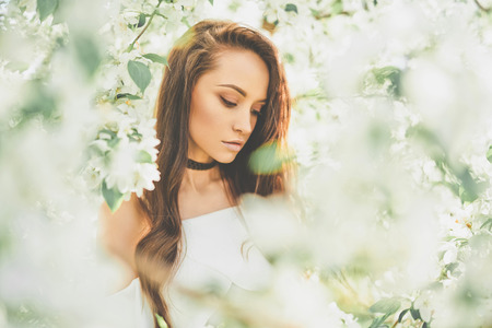 Outdoor fashion photo of beautiful young woman surrounded by flowers of apple-tree. Spring blossom. Summer vibesの写真素材