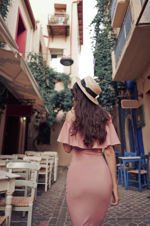 Beautiful brunette young woman wearing pink dress and straw hat walking on the street in old european Town. Fashion and style. Summer travelの写真素材